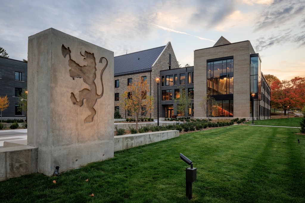 A decorative concrete wall stands in front of a new dorm building at sunset.